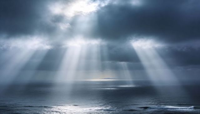 Piercing sunbeams cutting through dark clouds over moody ocean horizon