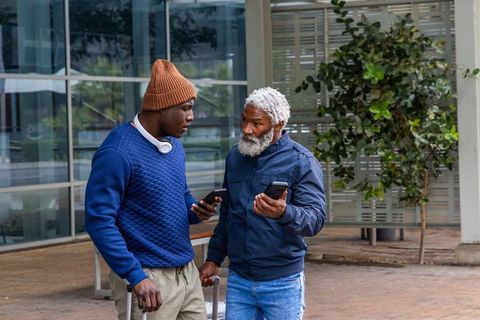 Comparing routes on smartphones while traveling through modern urban plaza with luggage