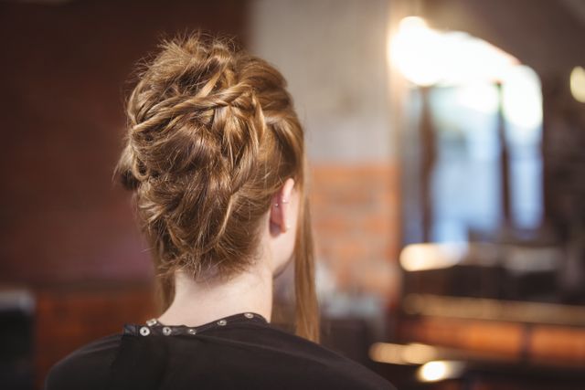 Woman with an intricate updo hairstyle seen from the back at a salon. Ideal for use in beauty and fashion magazines, hair care advertisements, and salon promotional materials.