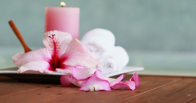 Ideal for promoting spa services, relaxation techniques, aromatherapy, and wellness products. This peaceful scene with a pink candle, a flower, towel rolls, and petals suggests a soothing and pampering atmosphere perfect for brochures, social media posts, and websites related to wellness and beauty.