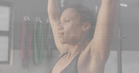 Mid adult woman lifting overhead in sunlit gym strength training focused athlete
