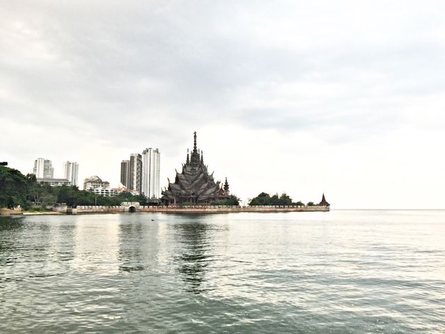 Wooden temple by tranquil waterfront with city skyscrapers in background. Perfect for travel articles, architectural studies, cultural landmark promotions, and contrast between traditional and modern themes.