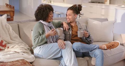 Young couple sitting on sofa holding coffee mugs enjoying cozy conversation in open-plan home