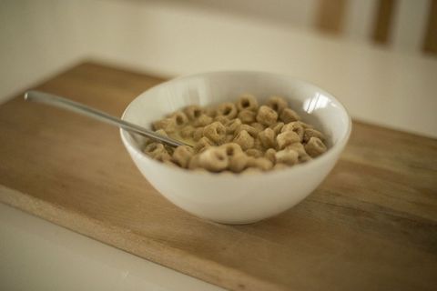 Warm morning breakfast bowl with whole grain o-shaped cereal and spoon on wooden board