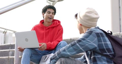Diverse college students on campus steps collaborating with laptop for outdoor study