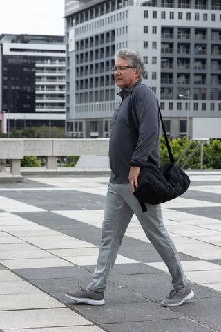 Senior man walking across urban plaza carrying duffel bag in gray activewear cityscape