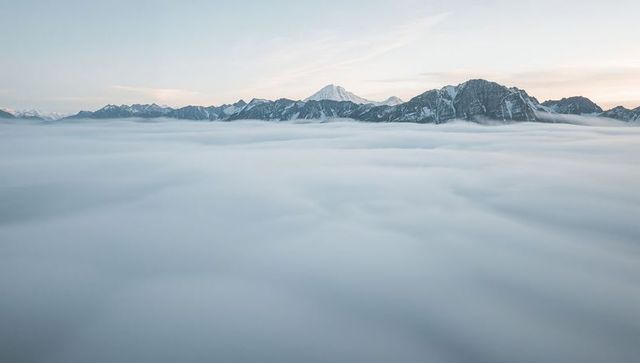 Rising snowcapped peak emerging above sea of clouds at pastel dawn panorama