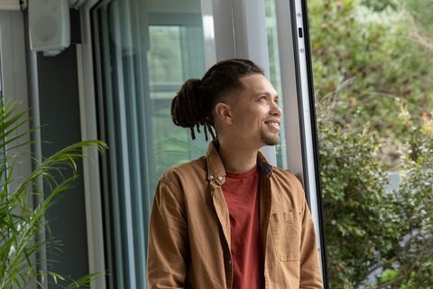 African american man standing by sliding door smiling, indoor greenery, natural light
