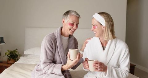Mature women enjoying at-home spa morning in robes with coffee mugs