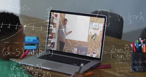 Boy attending remote math lesson on laptop while taking notes with colorful markers
