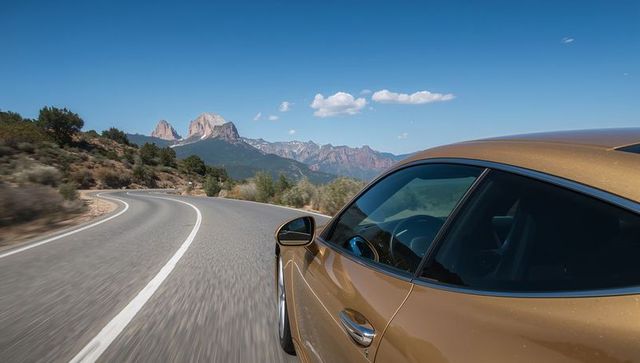 Driving gold coupe hugging winding mountain road with desert canyon vista, scenic curves and sheen
