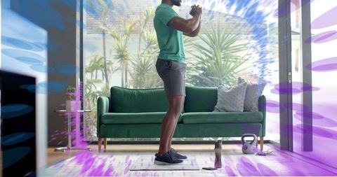 Man performing squat hold for home workout with kettlebell in bright living room
