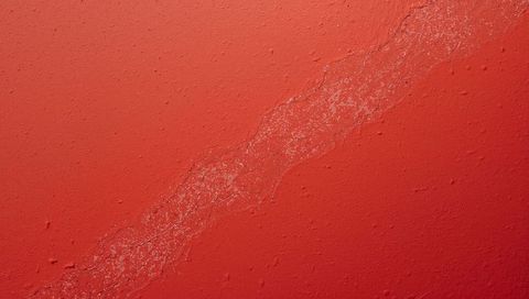Red peeling paint wall with diagonal crack, plaster texture and paint chips close-up