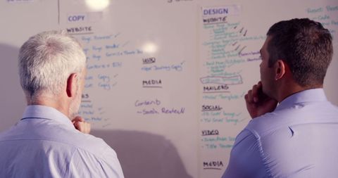 Businessmen analyzing strategies on whiteboard in office