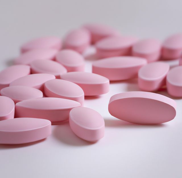 Close up of multiple pink pills laying on white background. Medicine, healthcare and treatment concept.
