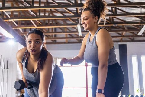 African american female trainer guiding client through dumbbell row strength workout