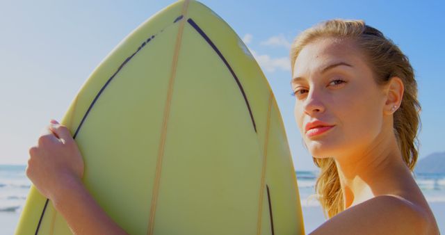 Young woman holding a surfboard while standing on a sunny beach. Great for illustrating summer activities, outdoor adventures, ocean lifestyle, and beach vacations. Ideal for travel blogs, adventure tourism, and sports marketing.