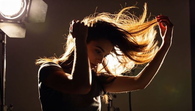 Posing female model fanning hair under studio backlight with dramatic rim light