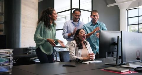 Diverse Team Celebrating Success Around Computer at Bright Office