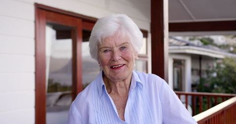Smiling Elderly Woman Standing on Balcony of Home