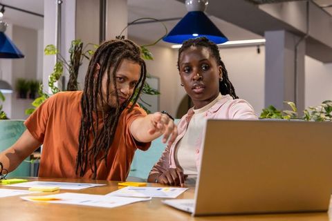 Coworkers collaborating over laptop, charts and sticky notes in modern open-plan workspace