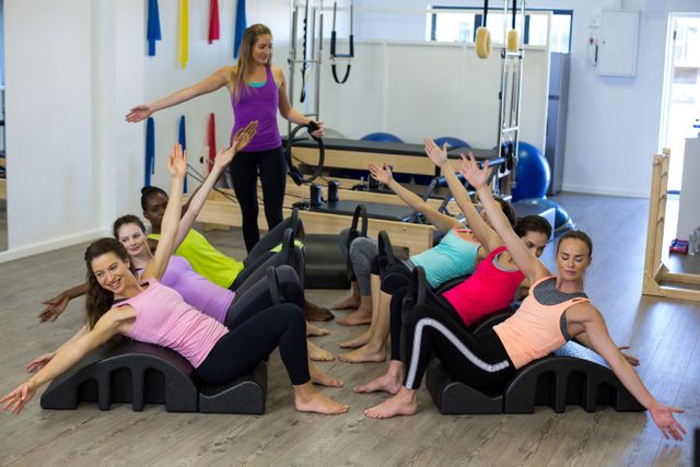 Female trainer guiding a group of women performing stretching exercises on arc barrels in a gym. Ideal for use in fitness blogs, gym advertisements, Pilates class promotions, and wellness articles.