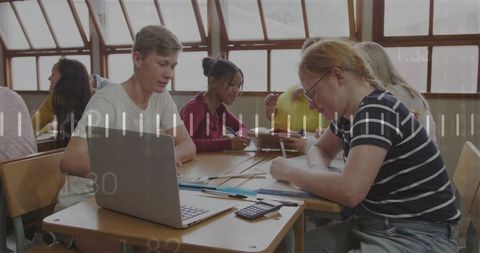 High school students collaborating with laptop and notebooks in sunny classroom