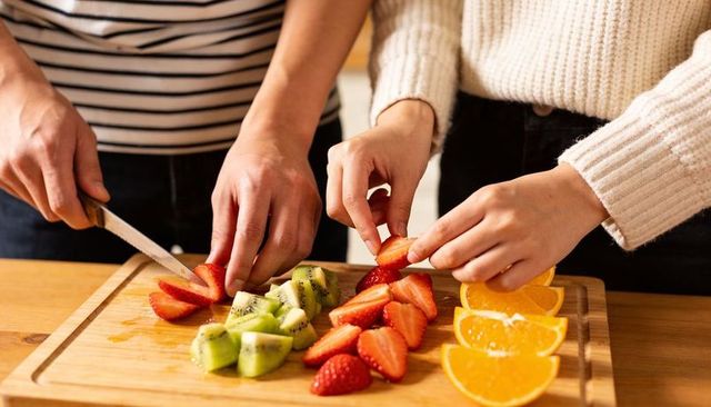 Couple slicing fresh fruit on wooden board, strawberries kiwi orange, hands preparing healthy breakf