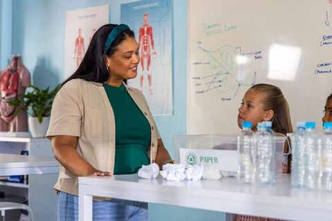 Female teacher guiding elementary students in hands-on biology lab with anatomy charts