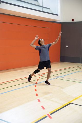 Asian teen athlete leaping on indoor gym court wearing knee brace