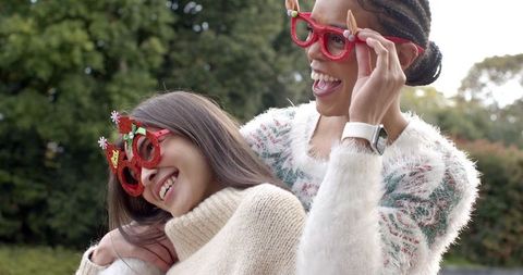 Diverse friends laughing in festive novelty glasses wearing cozy sweaters outdoors