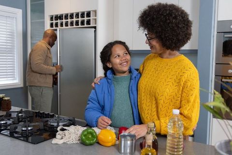 Mother helping daughter preparing vegetables at kitchen island while dad opening fridge