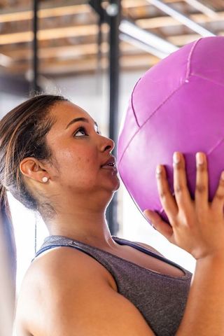 Holding purple medicine ball and focusing on core strength training in bright gym studio