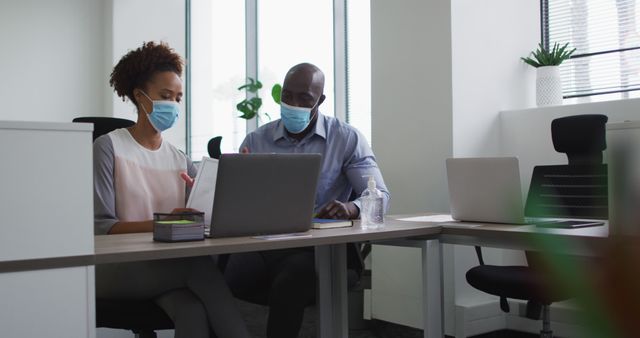 Diverse businessman and businesswoman in face masks discussing in office. business professional working in modern office during covid 19 coronavirus pandemic.