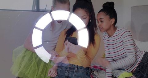 Teen girls sharing smartphone and trying clothes on bed with digital loading ring overlay