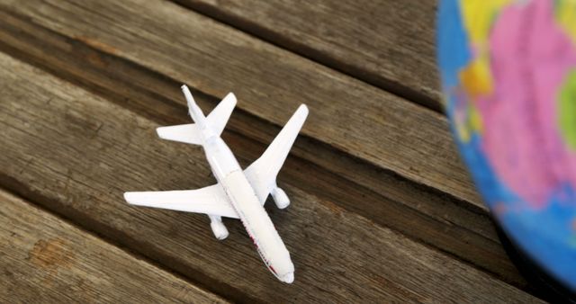 Toy airplane next to globe on wooden surface, symbolizing travel and adventure. Suitable for themes of global exploration, vacation planning, aviation industry, and educational purposes.