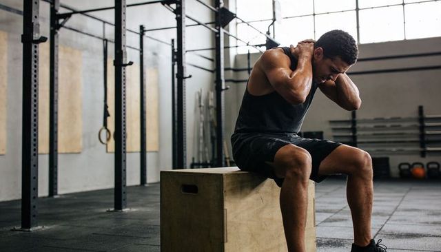 Tired athlete resting on plyo box in industrial gym after high-intensity workout session