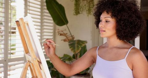 Woman Painting in Bright Home Studio Surrounded by Lush Plants