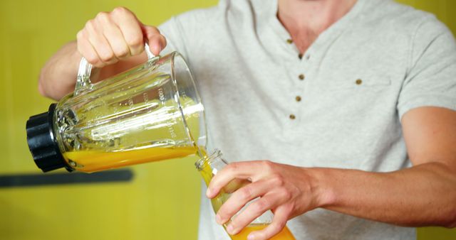 Man pouring freshly blended orange juice into bottle. Enjoying a homemade, healthy drink high in vitamin C. Perfect for illustrating concepts of healthy lifestyle, homemade beverages, and fresh juices.