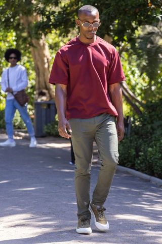 African american man walking in sunlit park wearing burgundy tee and olive pants