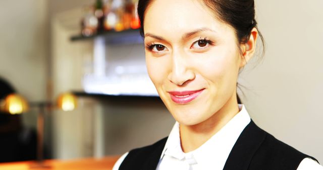 Young woman with Asian features wearing business attire smiling confidently at the camera in indoor work environment. Suitable for illustrating articles about professional success, workplace diversity, and career development. Perfect for corporate websites, career blogs, and HR materials.