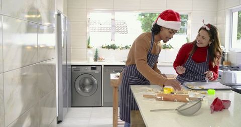 Couple baking festive christmas cookies on kitchen island with rolling pin and cutters