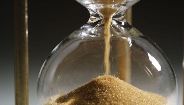 Golden sand streaming through glass hourglass closeup showing time passing and reflection