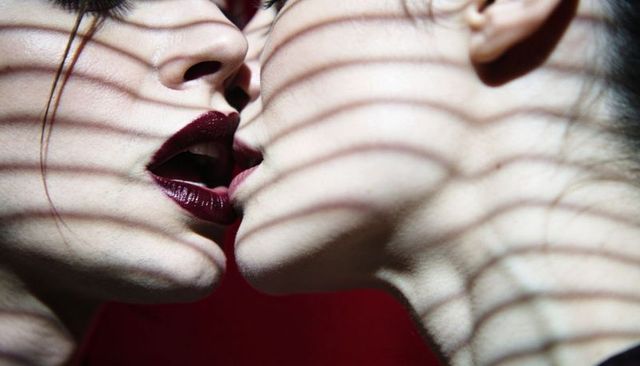 Two women kissing pressing lips with striped shadows and burgundy lipstick closeup