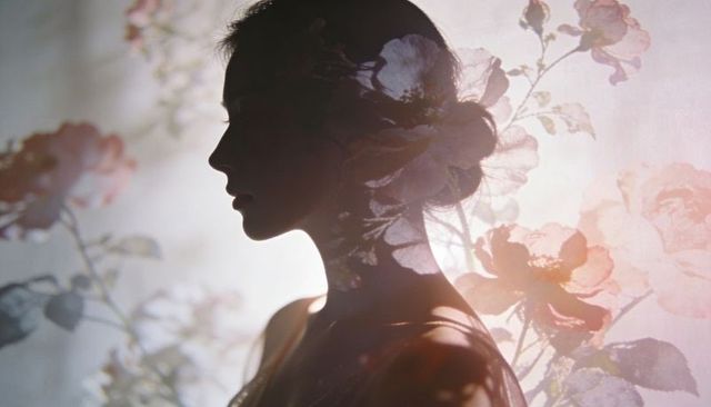 Silhouetted woman merging with projected floral blossoms, pastel double exposure portrait