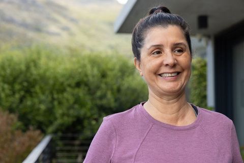 Smiling mature woman on home terrace wearing lavender top enjoying relaxed outdoor moment