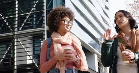 Diverse Female Friends Walking and Talking with Coffee outside Modern Glass Office Building