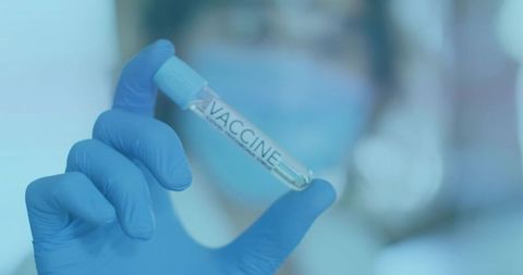 Healthcare worker holding vaccine vial labeled VACCINE while wearing blue gloves and mask