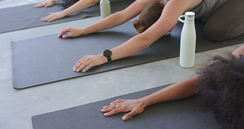 Diverse women stretching in yoga class on mats with water bottles and fitness wear
