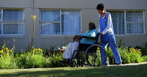 Nurse assisting senior man in wheelchair in garden setting